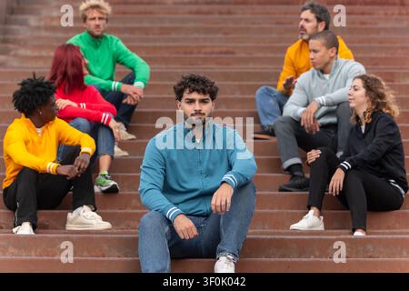 Groupe multiethnique de jeunes adultes assis sur des escaliers, chacun portant un sweat à fermeture éclair coloré. Ils discutent et affichent une attitude décontractée, tren Banque D'Images