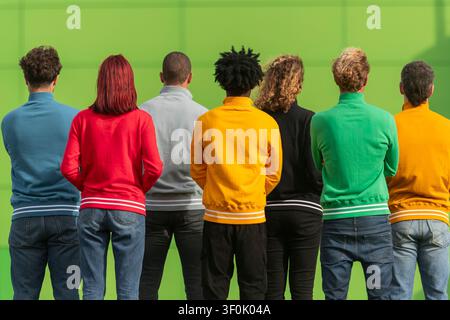 Un groupe divers de personnes en sweatshirts colorés se tient dos à dos. Les couleurs vives incluent le rouge, le bleu, le vert et le jaune, créant une li Banque D'Images