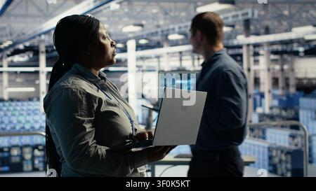 L'administrateur du centre de données utilise un ordinateur portable pour surveiller les processus d'apprentissage profond, en travaillant avec la technologie IA et les systèmes haute performance. Banque D'Images