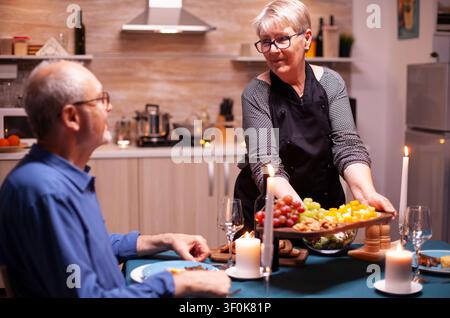 Couple de personnes âgées profitant d'un dîner romantique en cuisine, discutant à table tout en célébrant un anniversaire avec un repas chaud, illustrant une dînette domestique, une célébration de relation et un style de vie chaleureux en cuisine. Banque D'Images