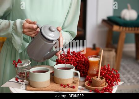 Jeune femme versant le thé viburnum savoureux de la théière dans la tasse à la maison Banque D'Images