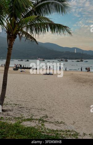 Da Nang, Vietnam - 29 avril 2026 : des gens se détendent sur la plage avec des bateaux de pêche traditionnels circulaires, la statue de la Dame Bouddha sur la montagne de la péninsule de Sơn Trà en arrière-plan Banque D'Images