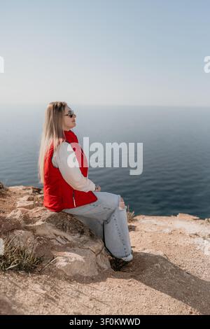 Femme au bord de la mer, assise au bord d'une montagne rocheuse tout en regardant l'horizon avec espace de copie Banque D'Images