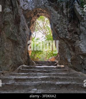 Escalier en pierre menant à travers une arche de grotte naturelle dans les montagnes de marbre à Da Nang, au Vietnam, avec des arbres de forêt luxuriants visibles en arrière-plan Banque D'Images