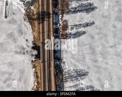 Vue aérienne d'une route traversant un lac gelé à Trakai, avec de longues ombres projetées par les arbres sur la glace enneigée, Trakai, comté de Vilnius, Lituanie. Banque D'Images