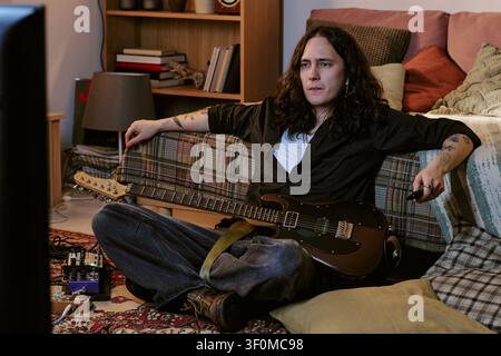 Musicien aux cheveux longs se détendant à la maison avec une guitare électrique Banque D'Images