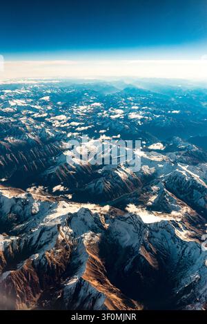Panorama aérien étendu capturé depuis une grande altitude au-dessus des Alpes européennes, révélant des sommets enneigés, des vallées glaciaires profondes et un lac alpin niché. Banque D'Images