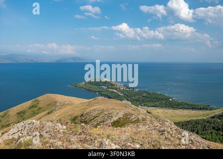 Vue panoramique depuis une crête de colline rocheuse surplombant les pentes herbeuses et la péninsule boisée de Sevan qui s'avance dans les eaux bleu profond de  Banque D'Images