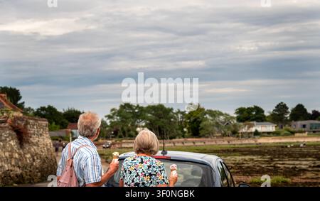 Un couple âgé vu de dos, profitant de cônes de glace sur Shore Road tout en regardant les vasières de marée basse du Bosham Creek. Banque D'Images