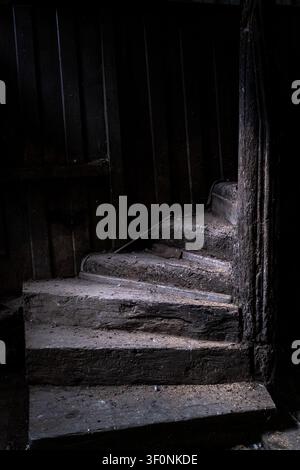 Vue intérieure d'un escalier en colimaçon en bois antique avec des lambris sombres, de la poussière et des traces d'incendie sur le bois à l'intérieur de la Maison de la Mere Pourcel Banque D'Images