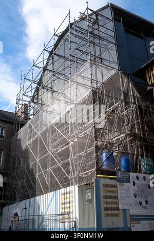 Vue extérieure du site de reconstruction de la Maison de la Mere Pourcel avec un important échafaudage métallique, des rideaux de protection en maille et des bidons de stockage bleus et Banque D'Images