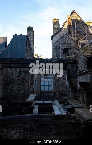 Vue extérieure du site de reconstruction de la Maison de la Mere Pourcel avec des murs en pierre, du bois carbonisé, des échafaudages et une couverture de toit temporaire en hauteur Banque D'Images