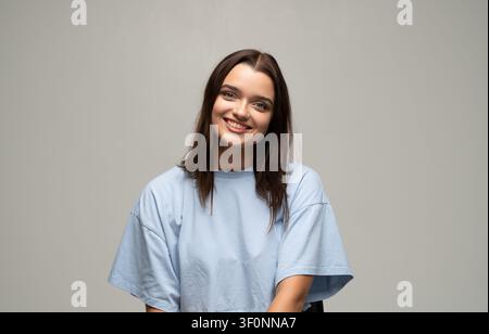 Jeune femme souriante, regardant l'appareil photo, exprimant la joie et la positivité dans un portrait de studio décontracté Banque D'Images