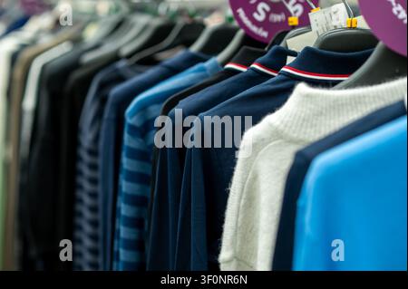 Gros plan des chandails bleus et blancs et des polos sur rack dans la rangée de magasin de mode de vêtements avec des étiquettes de rabais dans la boutique moderne pour la vente au détail Banque D'Images