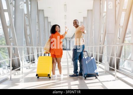 Couple noir heureux au terminal de l'aéroport se retournant et faisant des signes d'adieu Banque D'Images