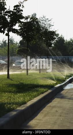 Arroseurs automatiques arrosant l'herbe verte dans un parc par une journée d'été ensoleillée, entretien rafraîchissant du paysage Banque D'Images