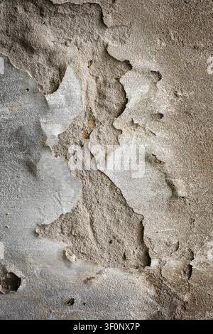 Texture d'une structure en béton endommagée. Vue détaillée du plâtre ébréché, de la vieille surface grise et du revêtement en ciment fissuré sur un mur en béton industriel. Banque D'Images