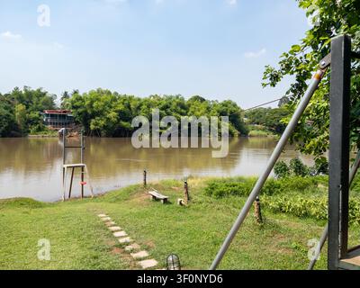 Installation de tyrolienne en plein air près d'une rivière calme entourée d'arbres verts luxuriants et de champs herbeux sous un ciel bleu clair. Banque D'Images