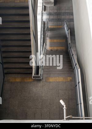 Vue par-dessus d'une escalier en béton avec des rampes en acier et des blocs de pavage tactile jaunes dans une station de transit moderne. Banque D'Images