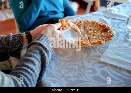 Mains tirant un morceau de pizza fromagère pendant un repas familial Banque D'Images