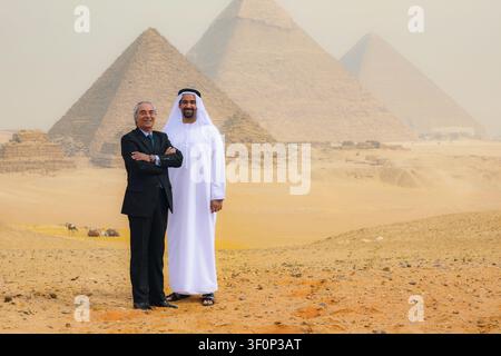 Portrait de partenariat commercial multiculturel d'un homme arabe en thobe et d'un cadre supérieur occidental souriant ensemble aux pyramides de Gizeh dans le désert égyptien, idéal pour Banque D'Images