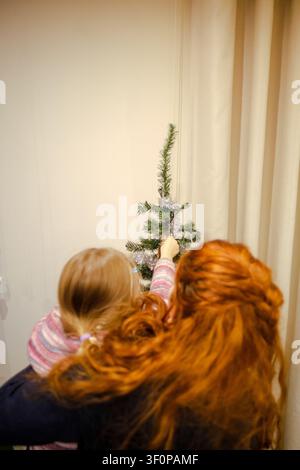 Des gens décorent un petit sapin de Noël artificiel, célébrant les fêtes d'hiver à la maison Banque D'Images