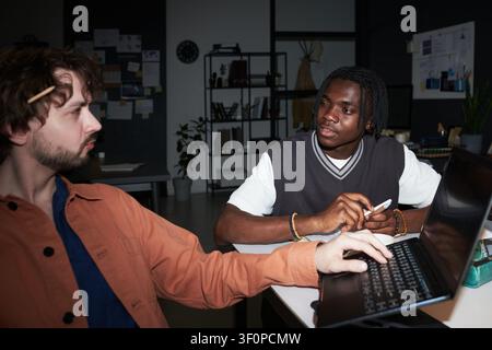 Jeune homme noir travaillant en collaboration avec un collègue masculin sur un ordinateur portable au bureau Banque D'Images