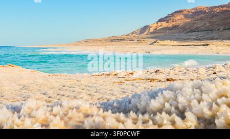 Close up de cristaux de sel de la mer Morte sur la plage du rivage en Jordanie au coucher du soleil avec une eau turquoise, côte désertique, point le plus bas du paysage terrestre. Jordanie - Israël Banque D'Images