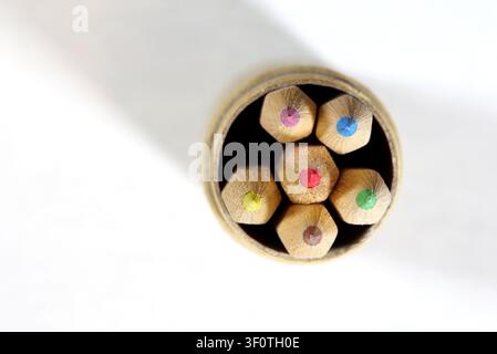 Vue de dessus de crayons de couleur dans un petit tube en carton sur fond blanc, six crayons d'art en bois avec des cœurs colorés, fournitures scolaires minimalistes soignées, Banque D'Images