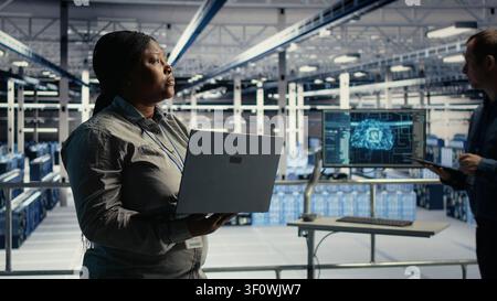 L'administrateur du centre de données utilise un ordinateur portable pour surveiller les processus d'apprentissage profond, en travaillant avec la technologie IA et les systèmes haute performance. Banque D'Images