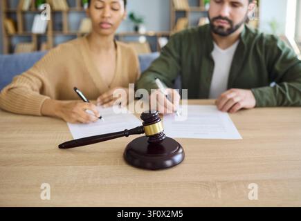 Couple signant des documents de divorce au bureau avec un marteau de tribunal, concept de séparation Banque D'Images