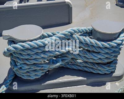 Corde d'amarrage bleue épaisse fixée autour des bittes métalliques du pont d'un navire Banque D'Images