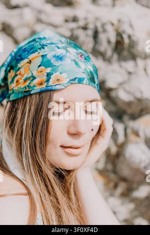 Portrait de femme avec foulard, jeune femme portant un foulard floral, se détendant les yeux fermés en plein air devant un fond rocheux Banque D'Images