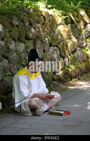 Nikko, Japon – 18 mai 2026 : Un participant vêtu de robes cérémonielles traditionnelles fait une pause à côté d'un mur de pierre couvert de mousse pendant le Hyakumono Banque D'Images