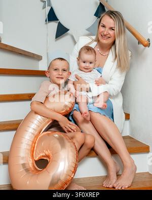 Famille assise ensemble, dans un escalier, avec ballon, couronne, avec escalier en bois, texture de tissu, d'une perspective en gros plan, avec blanc, bleu Banque D'Images