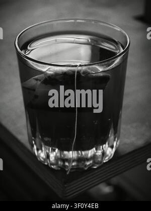 Un sachet de thé infusant dans une tasse en verre, créant une scène intérieure relaxante avec une ambiance calme et sereine. La vue de dessus met en valeur la beauté naturelle de th Banque D'Images