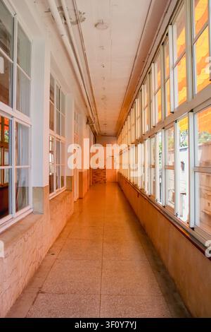 Vue en perspective d'un long couloir vide avec des rangées de fenêtres en verre et une lumière chaude du soleil. Banque D'Images