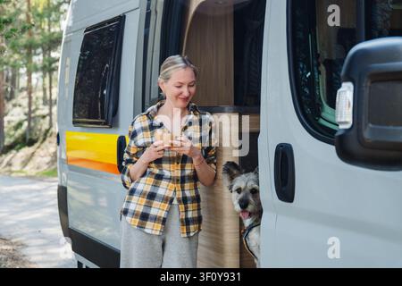 Une femme avec son chien savoure son café du matin près du camping-car Banque D'Images