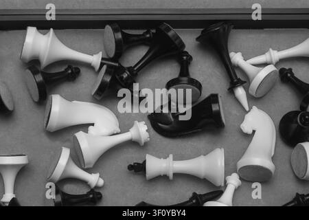 Un cliché en noir et blanc pris en contre-plongée d'un tas désordonné de pièces d'échecs blanches et noires posées dans une boîte ou un tiroir. Cette image monochrome conceptuelle Banque D'Images