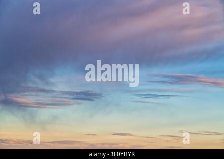 Ciel horizontal au coucher du soleil serein avec des nuages pastel doux dans des dégradés de violet, rose et or. Les transitions de couleurs douces créent une atmosphère rêveuse et tranquille. Banque D'Images