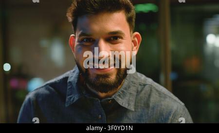 Portrait de tête d'un homme d'affaires indien optimiste souriant et regardant la caméra dans un bureau le soir. Homme d'affaires arabe, professionnel hindou Banque D'Images