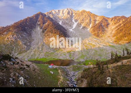 Une vue aérienne du paisible lac Kareri niché sous des sommets montagneux rocheux imposants dans l'Himachal Pradesh, en Inde. Banque D'Images
