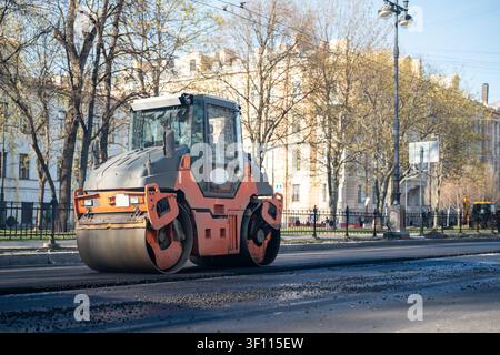 Rouleau de route sur la rue compresse l'asphalte fraîchement posé sur la route de circulation, travaux de construction en ville. Banque D'Images
