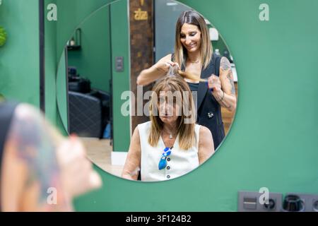 Coiffeur peignant les cheveux d'une femme, vus en reflet dans un miroir rond Banque D'Images