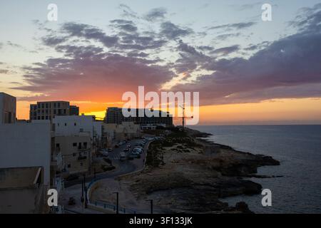 Beau coucher de soleil doré sur les bâtiments de la ville côtière et le rivage rocheux à Malte. Banque D'Images
