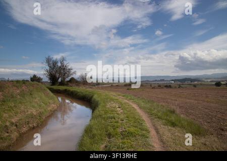 Sentier de terre serpentant à travers des terres agricoles à côté d'un canal d'irrigation avec des collines en arrière-plan Banque D'Images