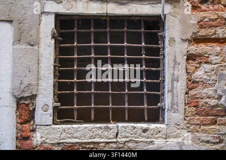 Fenêtre à grille métallique rouillée dans un mur de pierre et de brique vieilli. Témoignages d'usure et de temps Banque D'Images