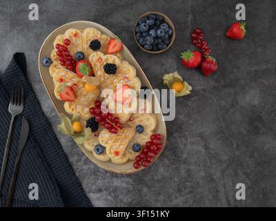 Composition de petit-déjeuner en hauteur mettant en vedette des gaufres à pancake garnies de baies fraîches et de fruits de saison Banque D'Images