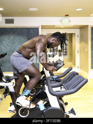 Bel homme, jeune et musclé, Afro-Américain, un bodybuilder, faisant du vélo stationnaire dans la salle de sport Banque D'Images