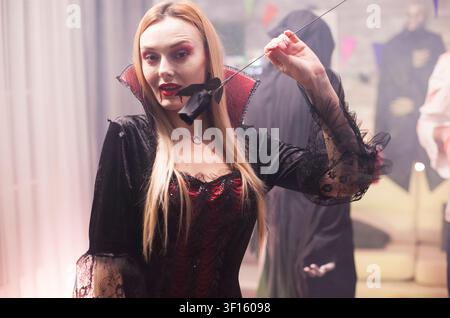Jeune femme déguisée en vampire effrayant célèbre Halloween avec un groupe de personnes en costumes, montrant un style d'horreur ludique, activité de groupe d'amis. Banque D'Images